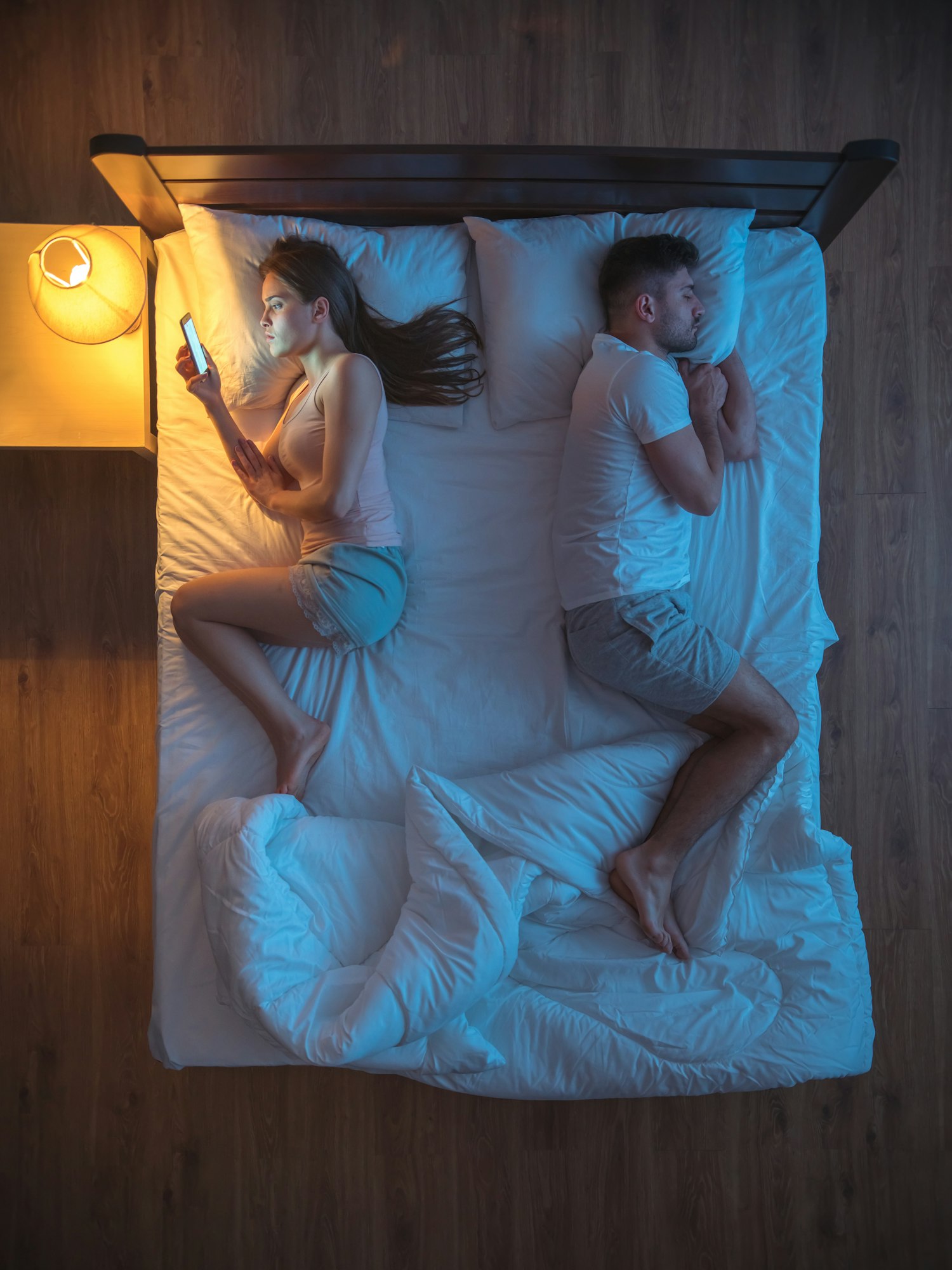 The sad couple with smartphone lay on the bed. night time. view from above,